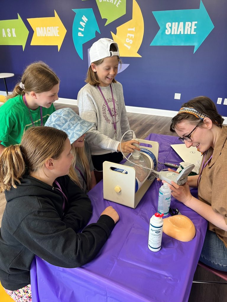 person sitting at a table with four kids using an ultrasound wand to study what's inside a clear cylinder